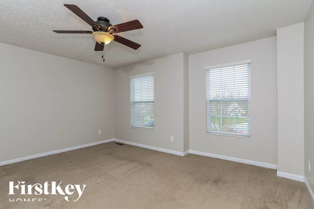 A room with a ceiling fan and two windows.