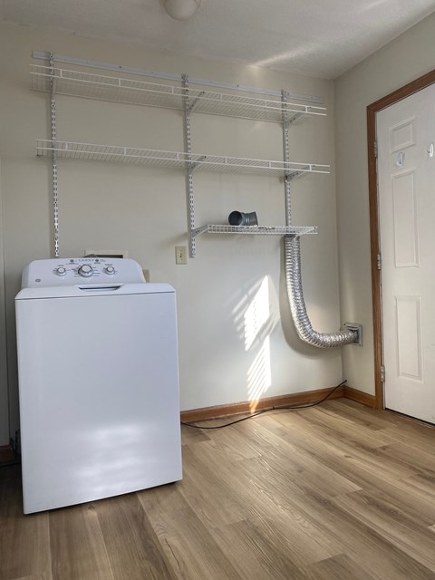 A white dishwasher is in a kitchen with a white wall and a white door.