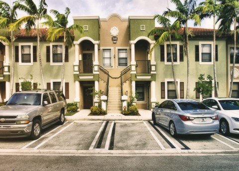 A silver truck is parked in front of a two-story building with a balcony.