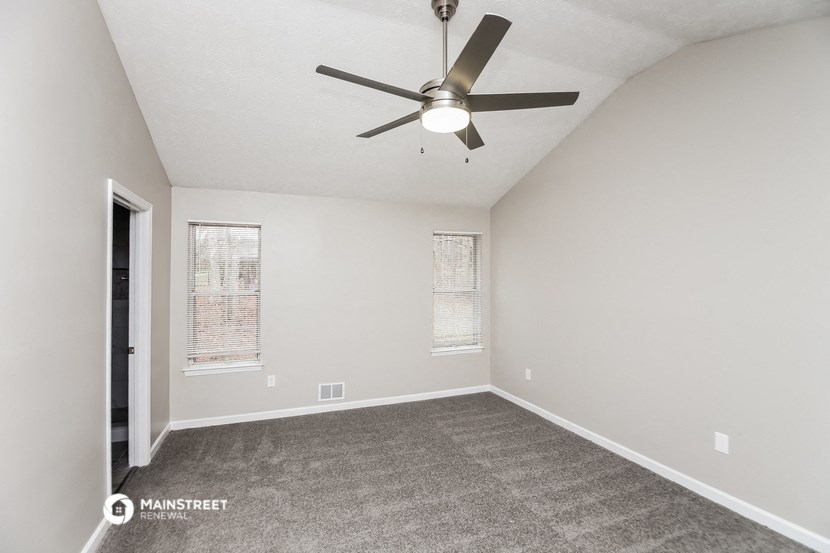 the spacious living room with carpet and a ceiling fan