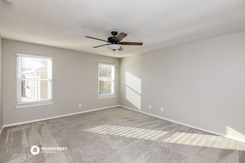 the spacious living room with ceiling fan and windows