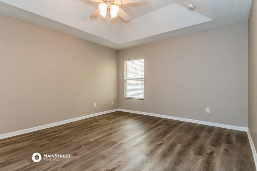 the spacious living room with hardwood flooring and a ceiling fan