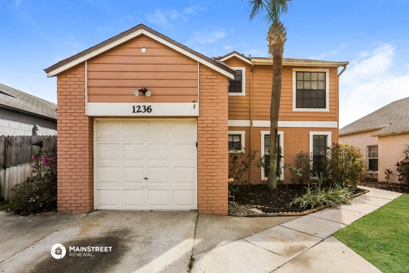 a tan house with a white garage door in front of a palm tree