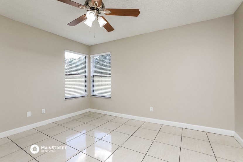the spacious living room has a ceiling fan and tiled floors