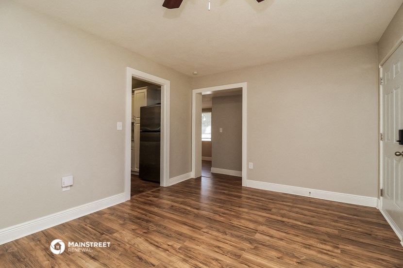 an empty living room with wood flooring and a door to a hallway