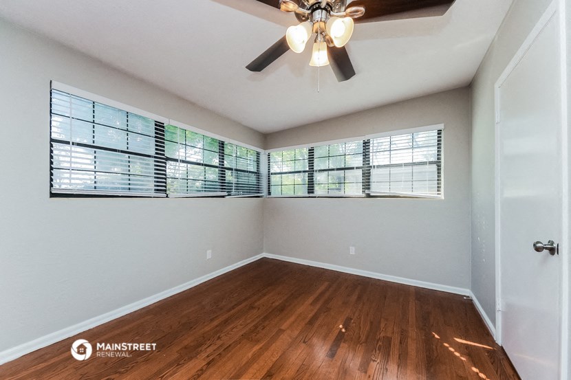 an empty living room with windows and a ceiling fan