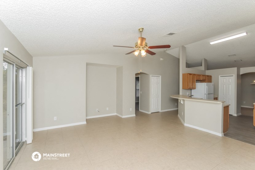 an empty living room with a ceiling fan and a kitchen