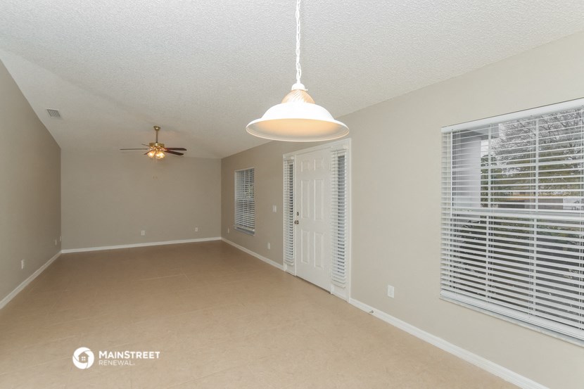 a spacious living room with large windows and a ceiling fan