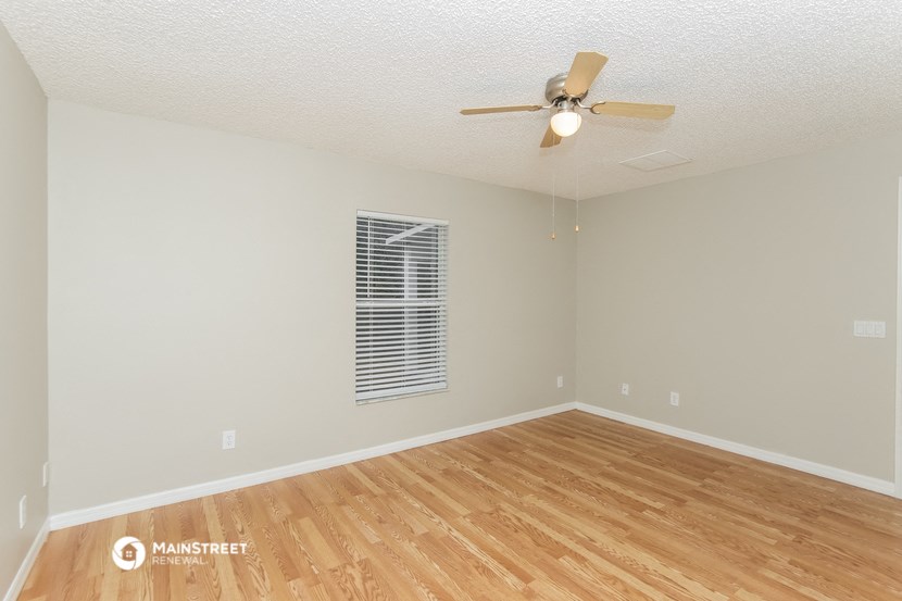 the spacious living room with hardwood flooring and a ceiling fan
