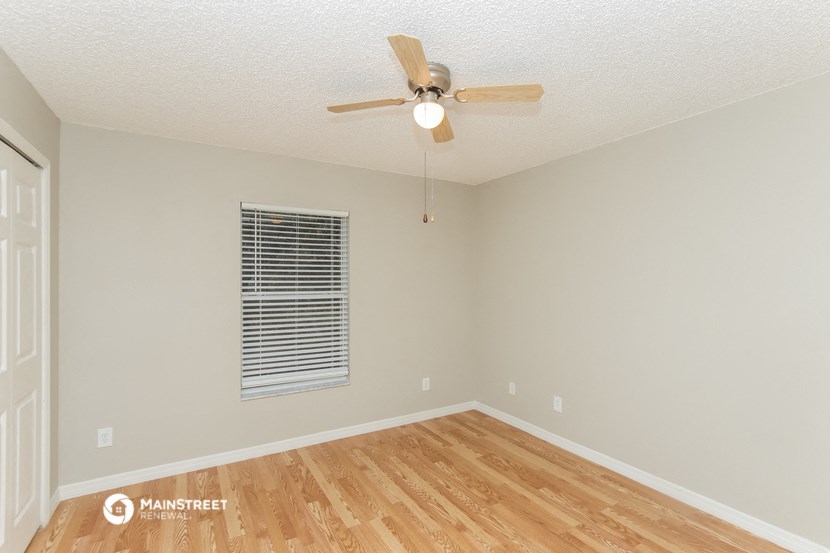 the spacious living room with hardwood flooring and a ceiling fan