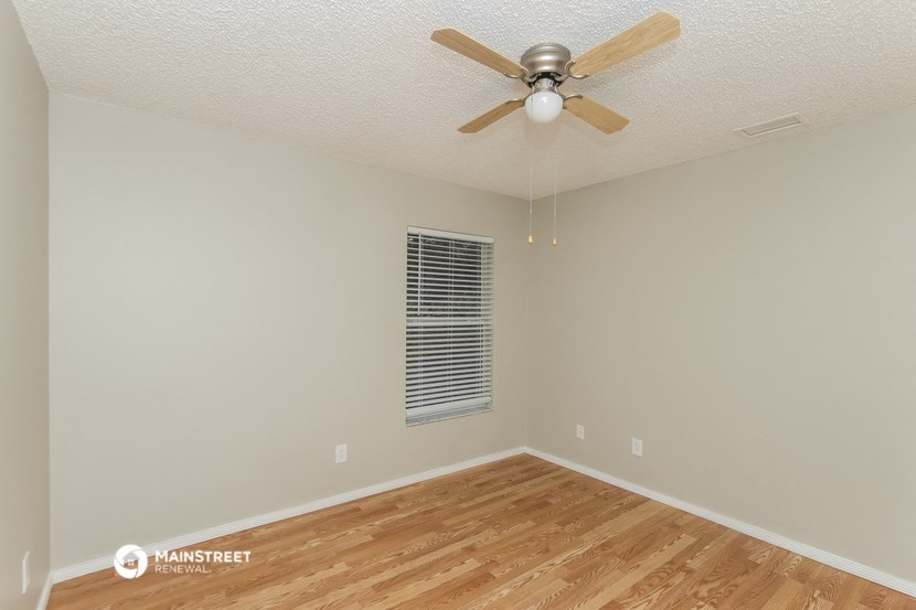 the spacious living room with hardwood flooring and a ceiling fan
