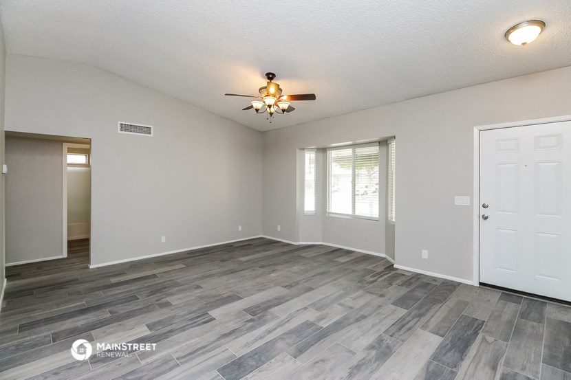 the spacious living room with a ceiling fan and a door to the bedroom
