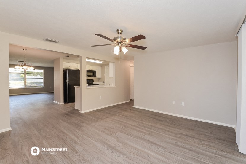 an empty living room with a ceiling fan and a kitchen