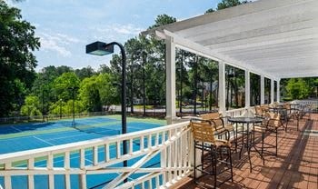 A pool with a white fence and chairs under a roof.