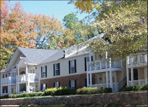 A white house with a balcony and a stone wall in front.