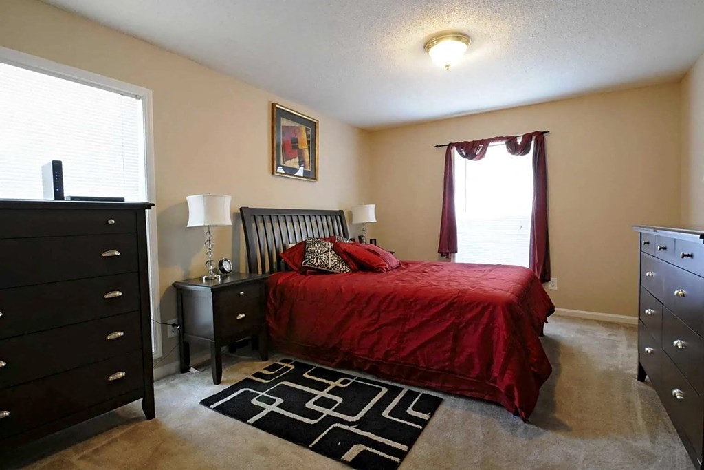A bedroom with a red bedspread and a black and white rug.