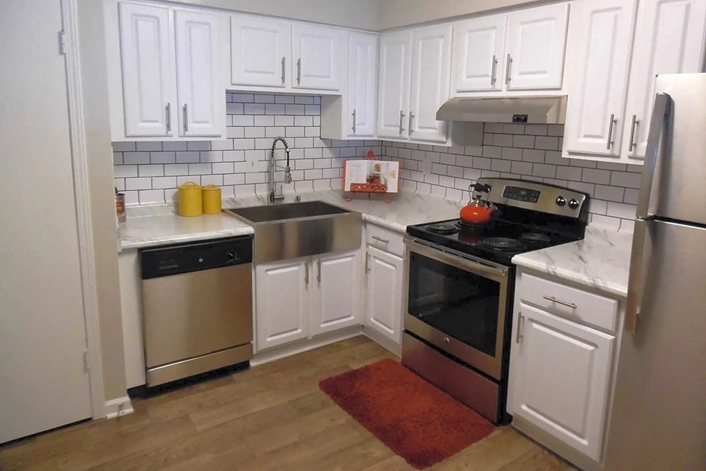 A kitchen with white cabinets and a red rug on the floor.