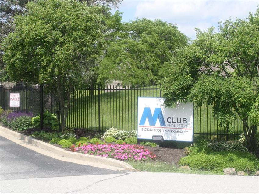 a sign in front of a fence with trees and flowers
