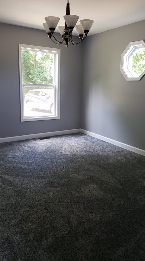 A room with a grey carpet and a chandelier.