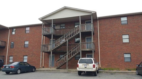 a brick apartment building with stairs and cars in a parking lot