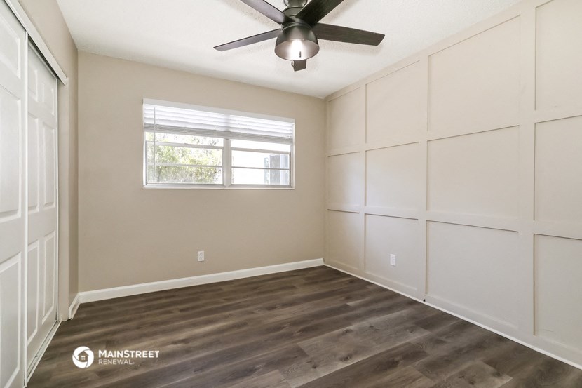 the spacious living room with white walls and a ceiling fan