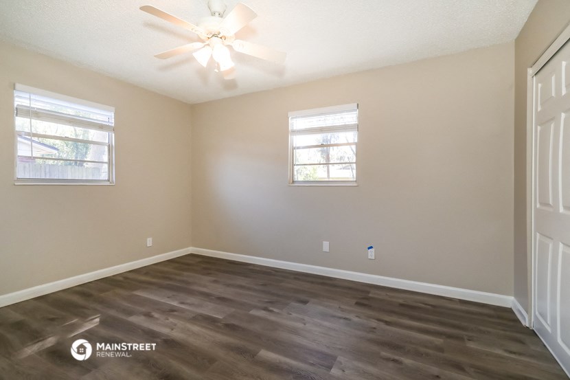 the spacious living room with hardwood flooring and a ceiling fan