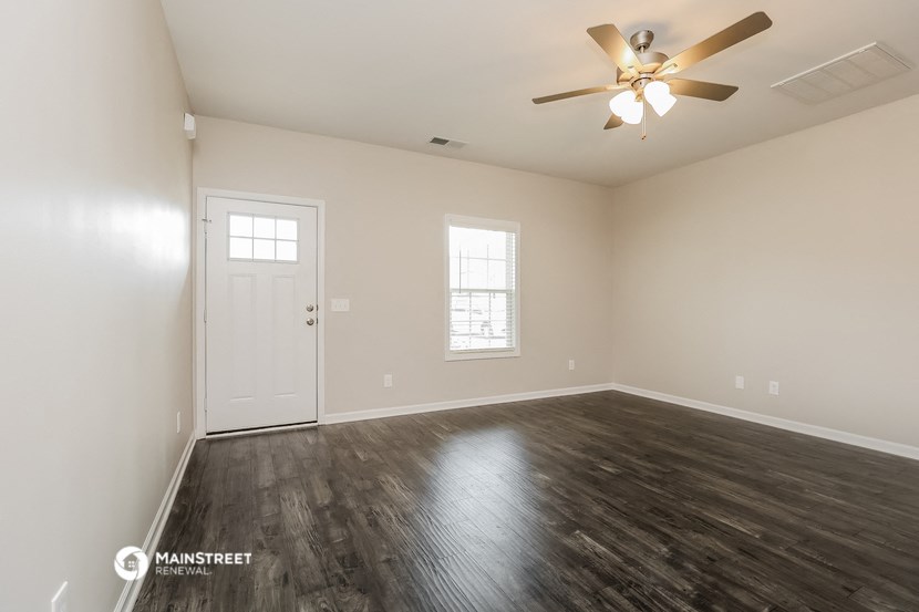 the spacious living room with wood flooring and a ceiling fan