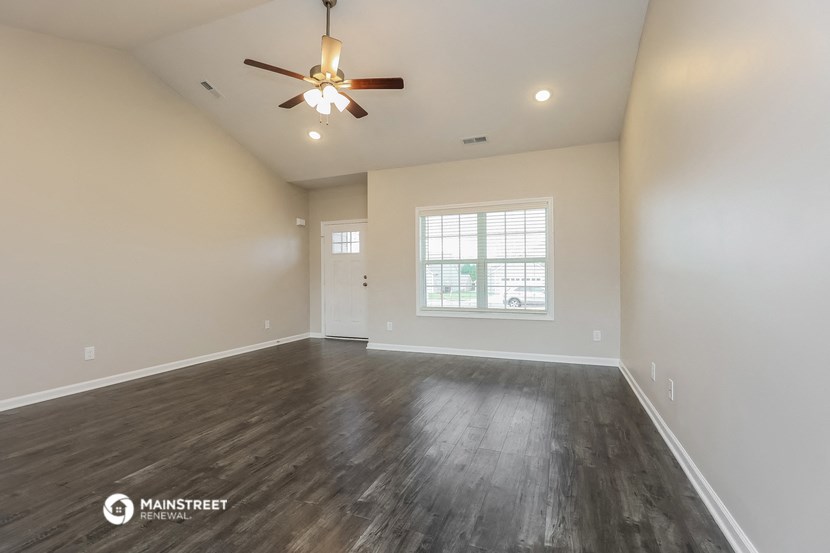the spacious living room with wood flooring and a ceiling fan