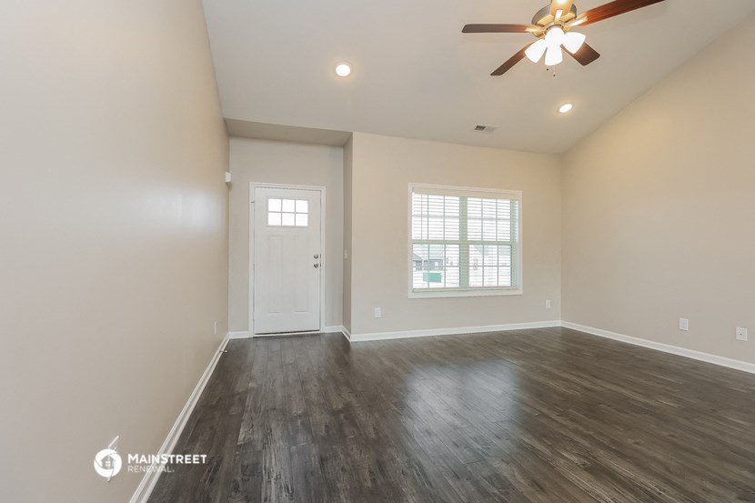 the spacious living room with hardwood flooring and a ceiling fan