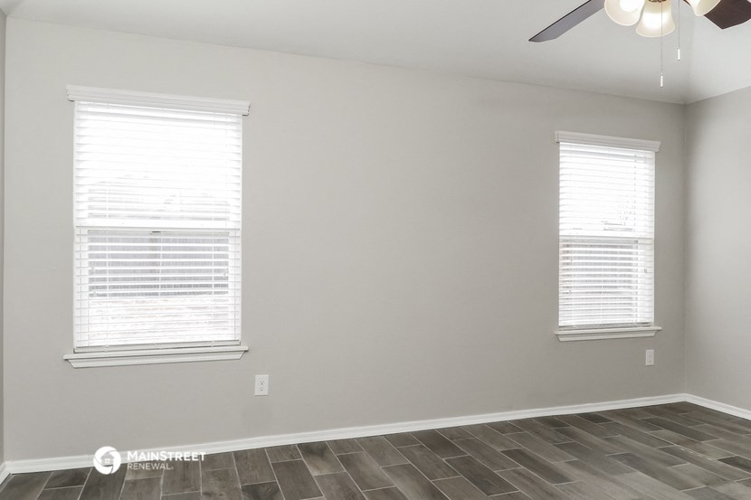 the spacious living room with two windows and a ceiling fan