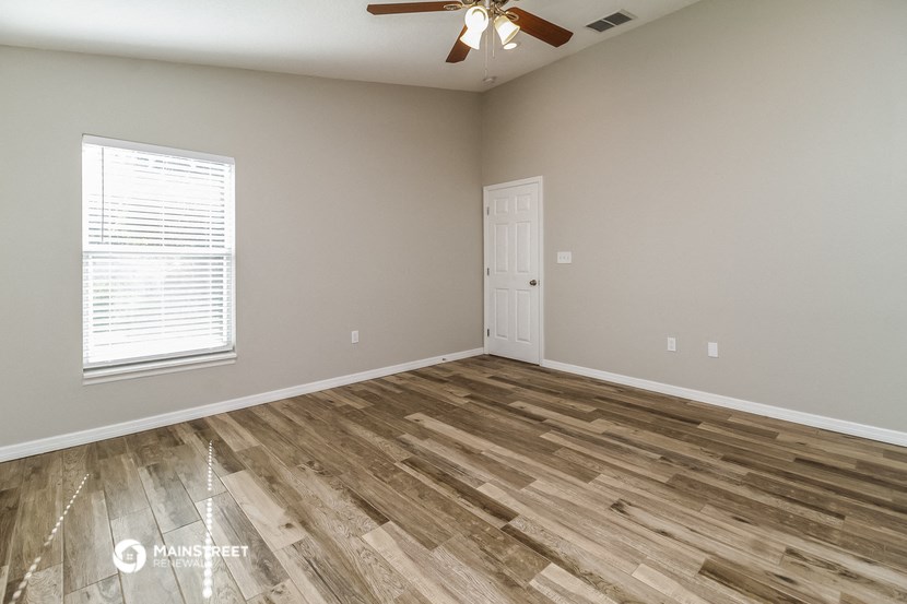 the spacious living room with wood flooring and a ceiling fan