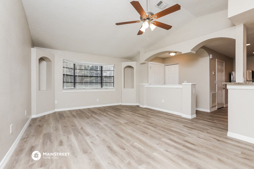 an empty living room with a ceiling fan and a kitchen