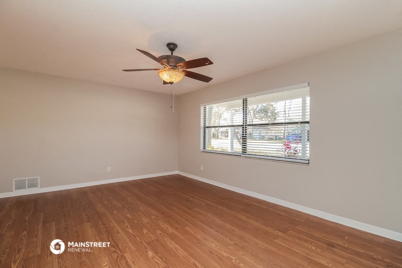 the spacious living room with wood floors and a ceiling fan