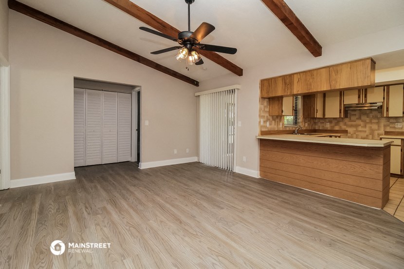 an empty living room with a ceiling fan and a kitchen