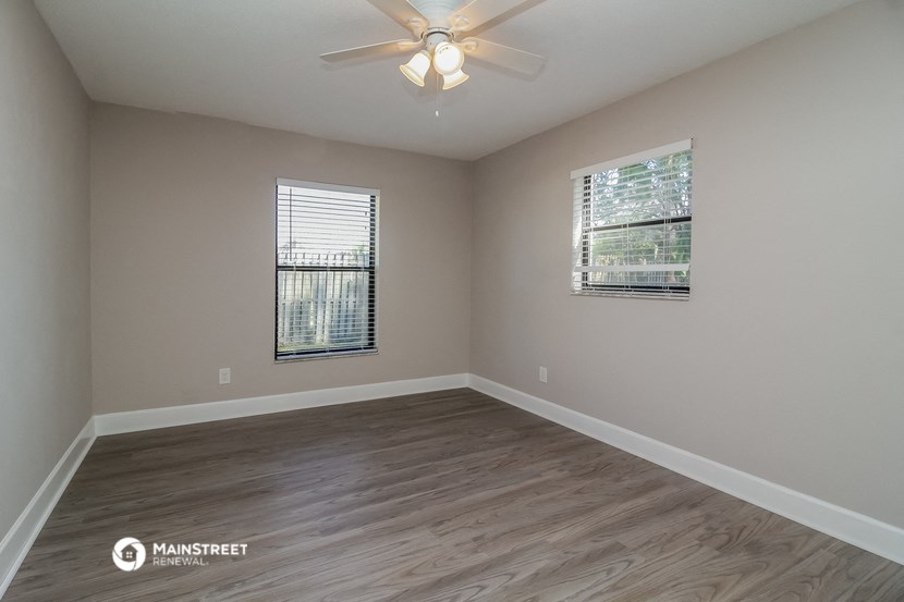 the spacious living room with hardwood flooring and a ceiling fan