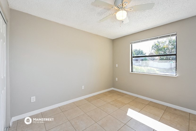 an empty living room with a large window and a ceiling fan