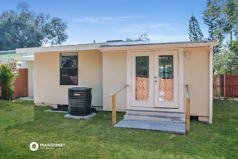 the exterior of a small tan house with a backdoor and a grassy yard