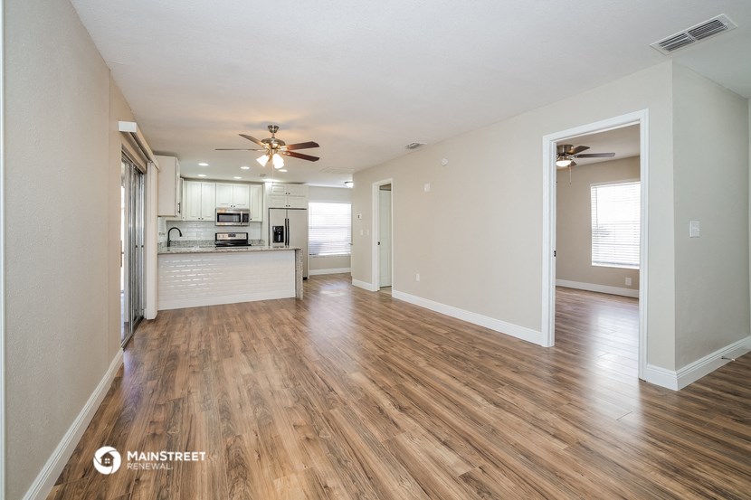 an empty living room and kitchen with wood flooring and a ceiling fan