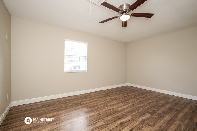 the spacious living room with wood flooring and a ceiling fan