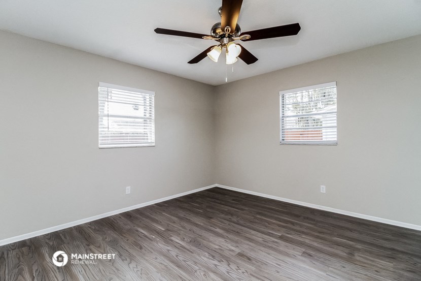the spacious living room with wood flooring and a ceiling fan