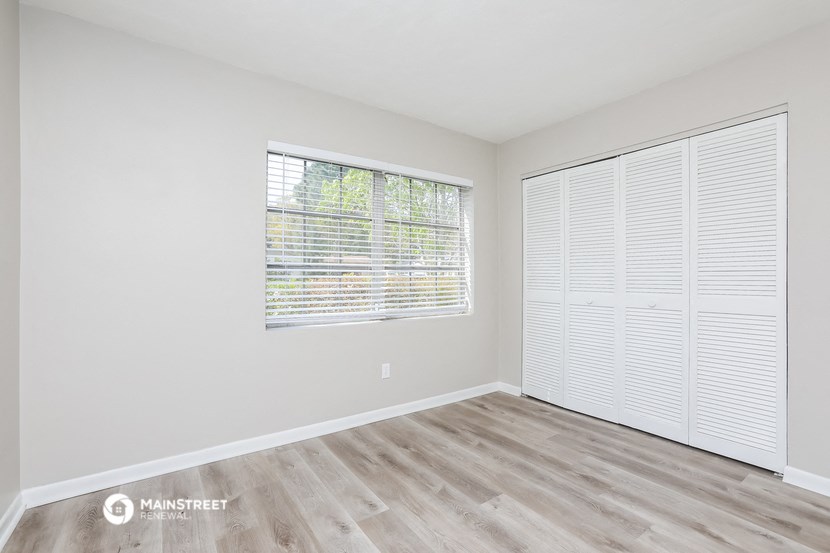 a spacious living room with a large window and wood flooring
