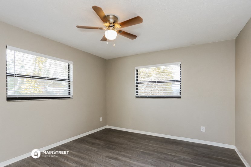 the spacious living room with a ceiling fan and two windows
