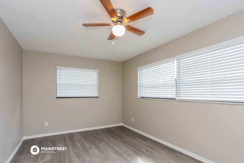 the spacious living room with a ceiling fan and two windows