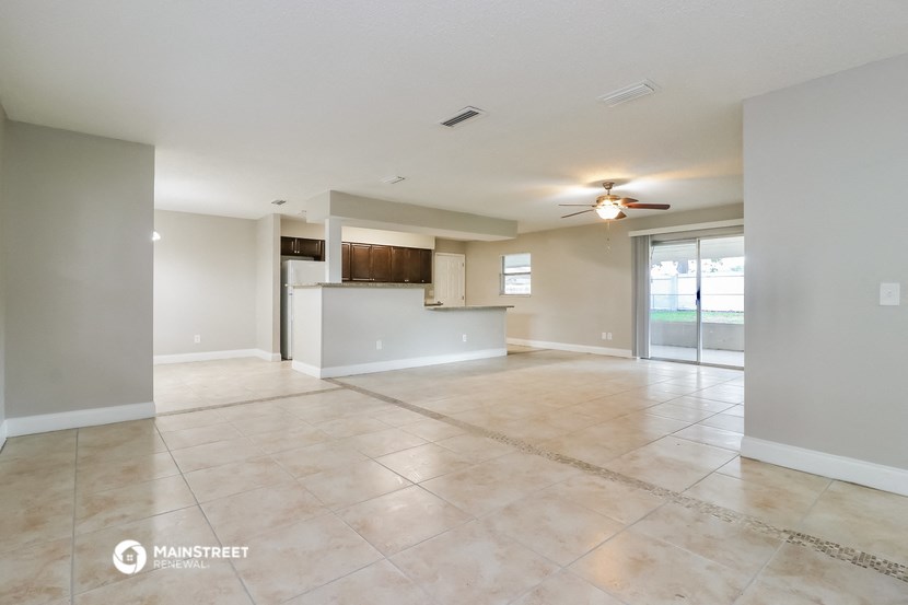 an empty living room with a kitchen and a ceiling fan