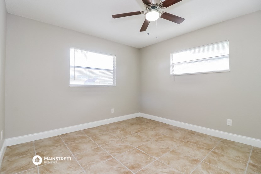 an empty room with a ceiling fan and two windows
