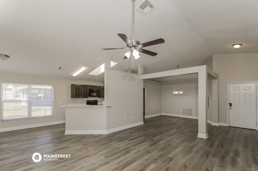 the living room and kitchen of an empty house with a ceiling fan