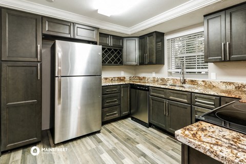 a kitchen with black cabinets and granite counter tops and stainless steel refrigerator