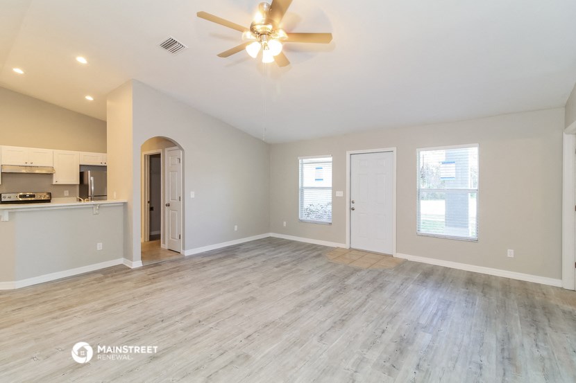 an empty living room with a ceiling fan and a kitchen