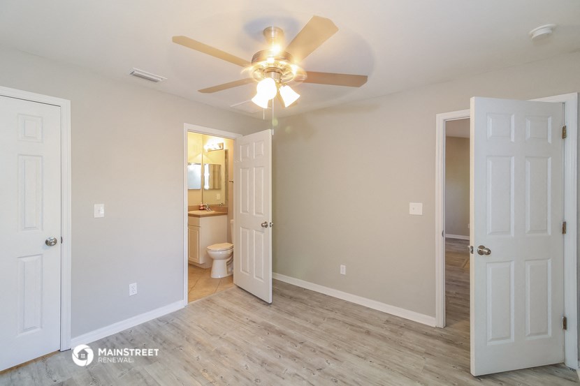 a bedroom with a ceiling fan and a door to a bathroom