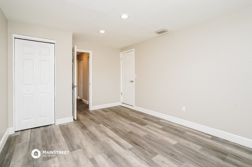 the spacious living room with wood flooring and a door to the hallway